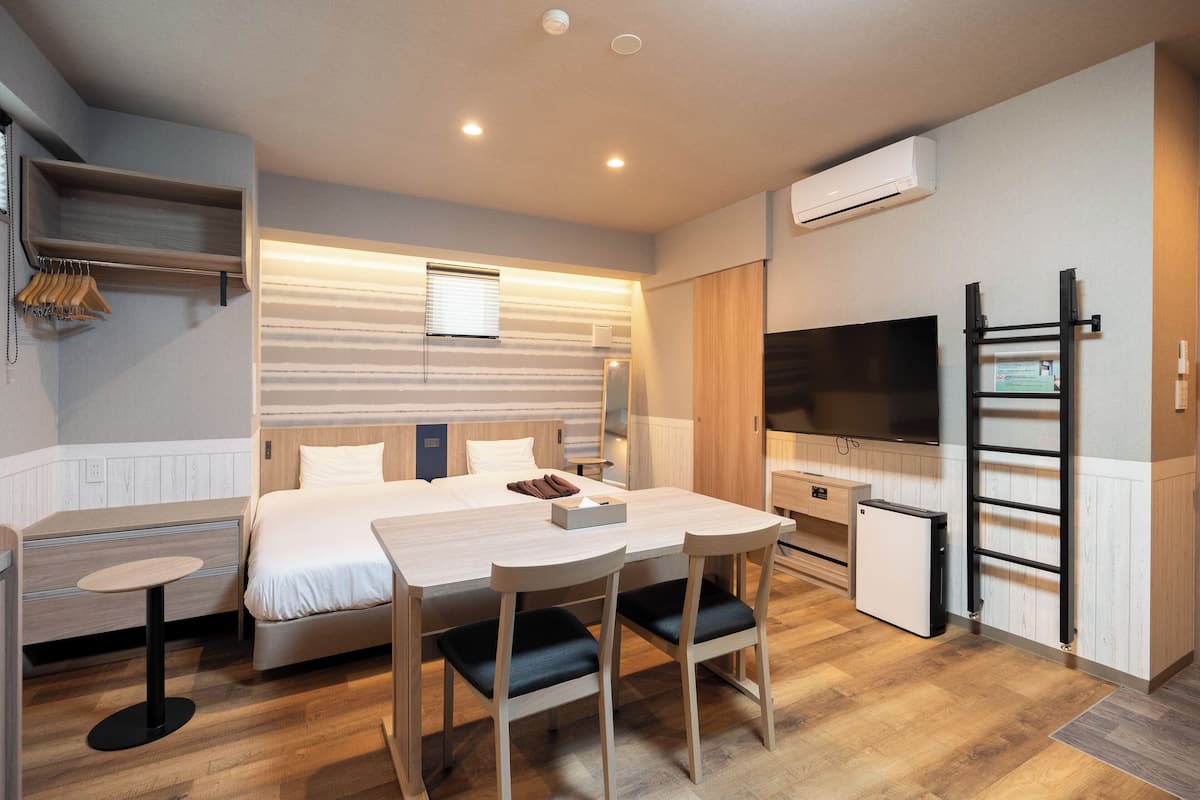 A compact hotel room with a bed, a small desk, a chair, a TV, and a mini-fridge.