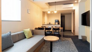 Et moderne hotelværelse med en sofa, et rundt bord og et fjernsyn ophængt på væggen.