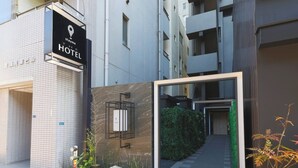 En hotelindgang med moderne design, inklusive et skilt, et lille haveområde og en sti til indgangen.