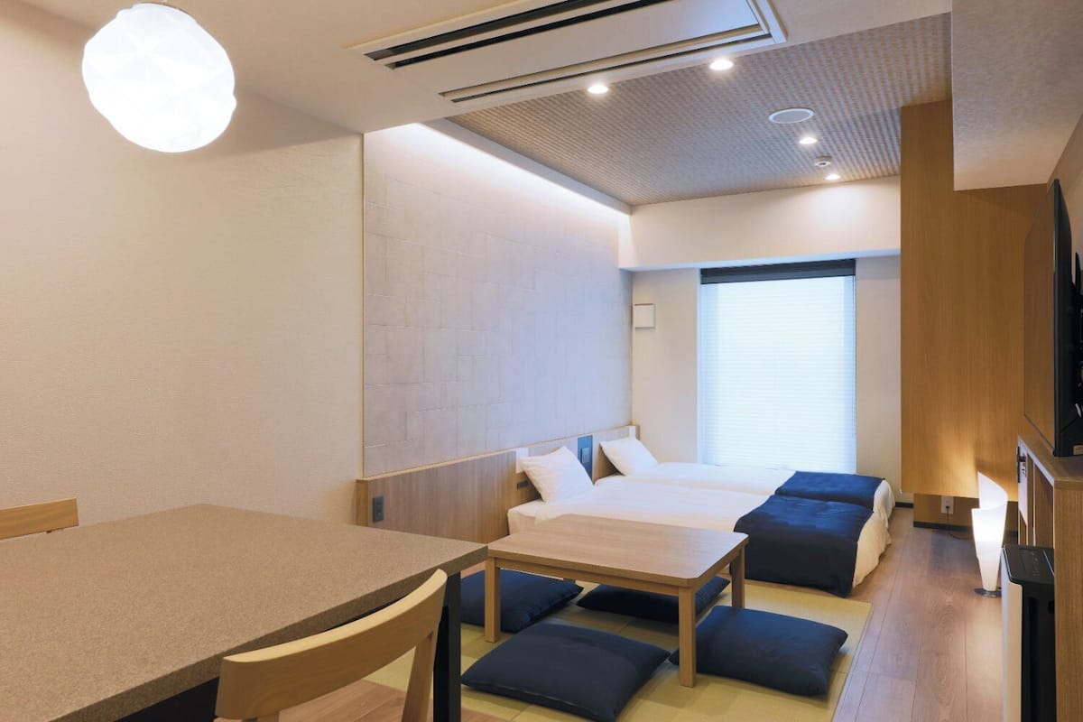 A hotel room with two beds, a dining table, and a TV.