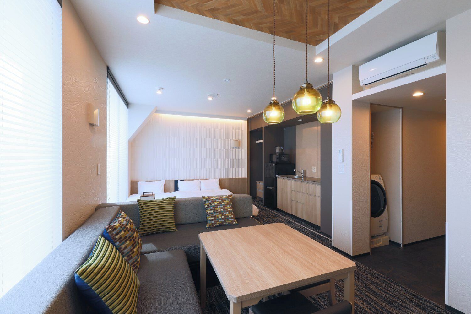 Une chambre d’hôtel moderne équipée d’un canapé, d’une table en bois, d’un coin cuisine et d’un lave-linge.