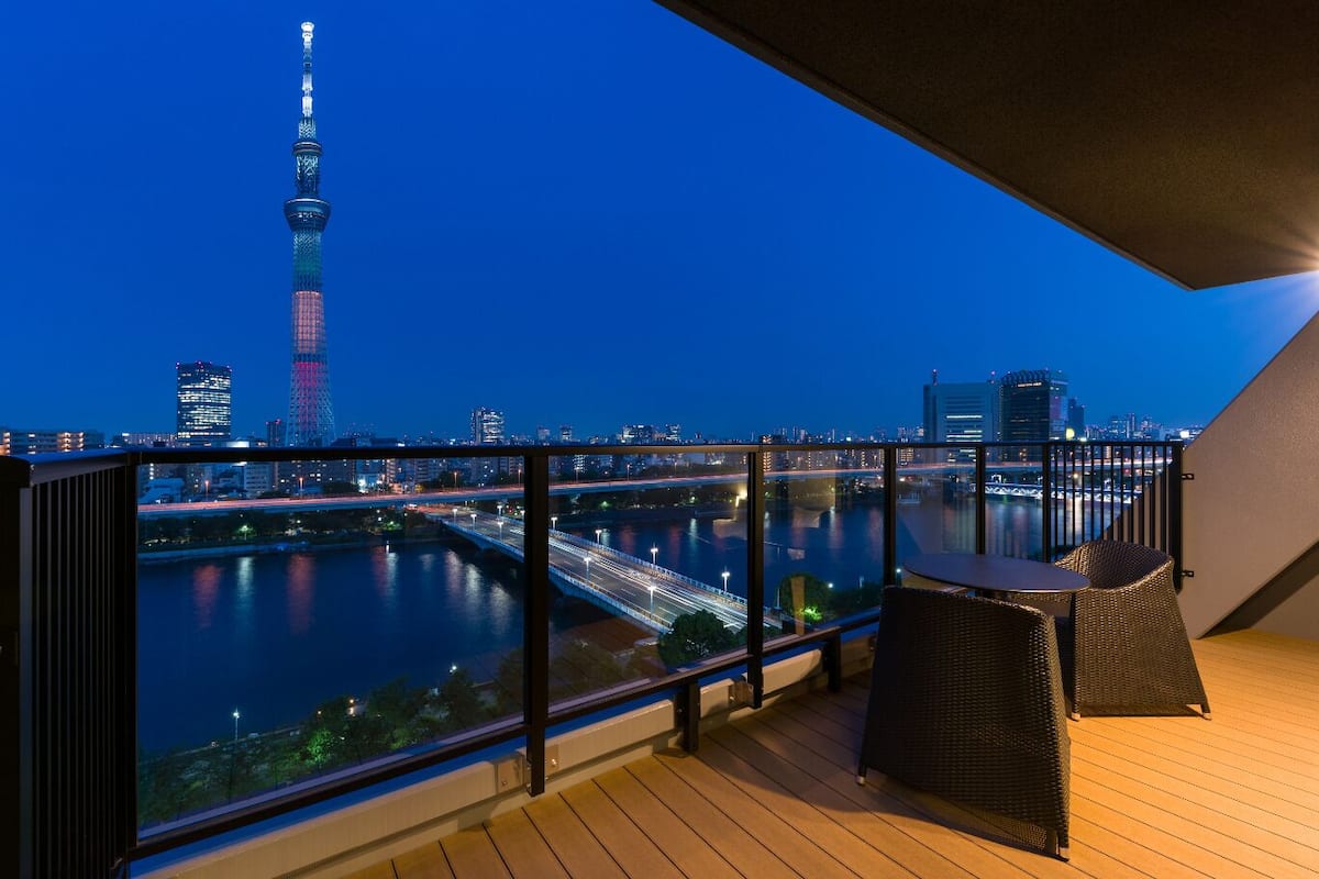 A balcony with a view of a river and a city skyline, including a tall tower.
