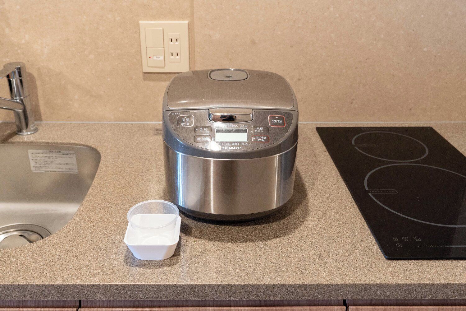 A kitchen with a rice cooker, a small white container, and a black induction cooktop.