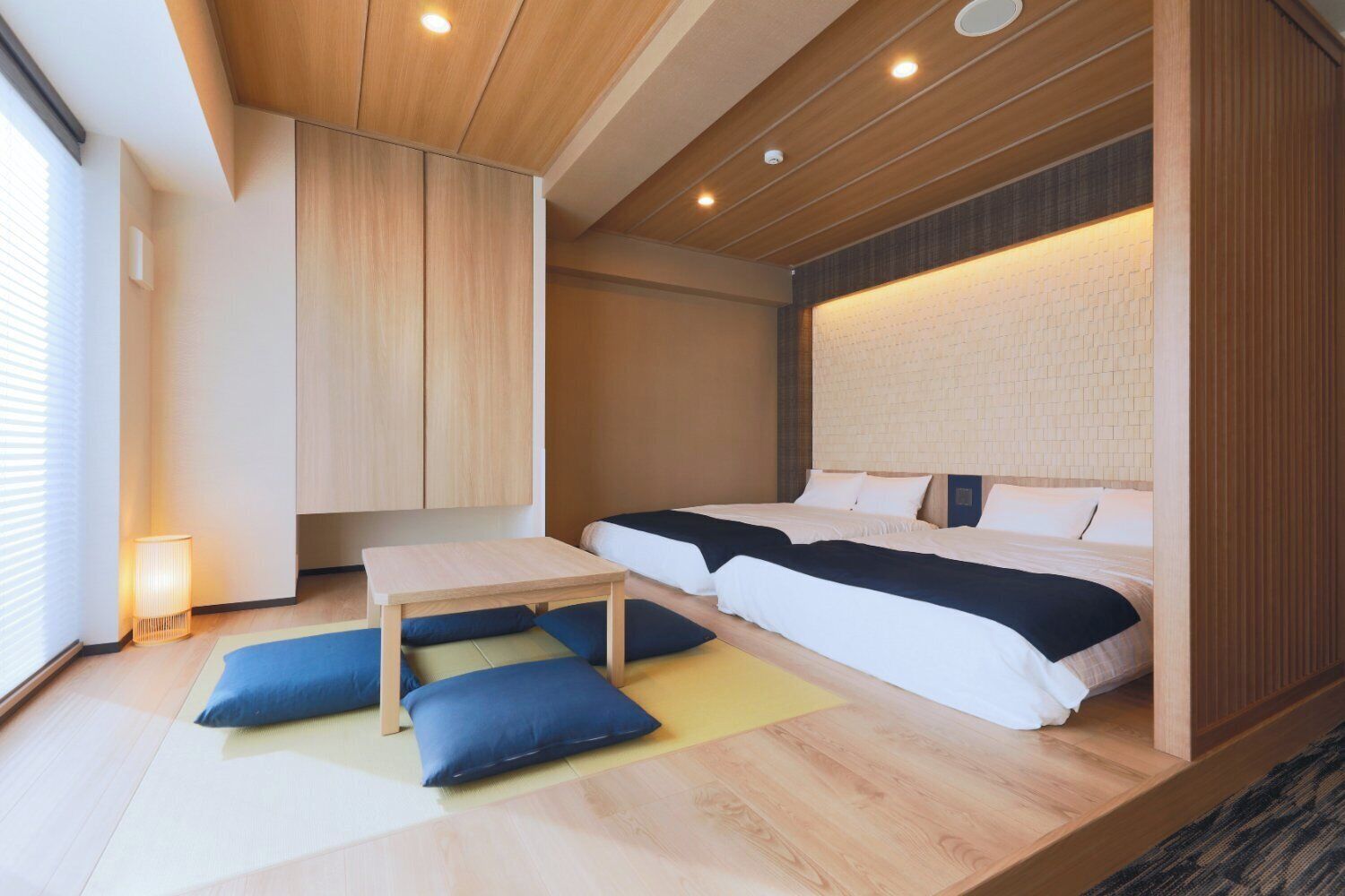 Ein modernes Hotelzimmer mit einem großen Bett, einem kleinen Tisch und einer Sitzecke mit Kissen.
