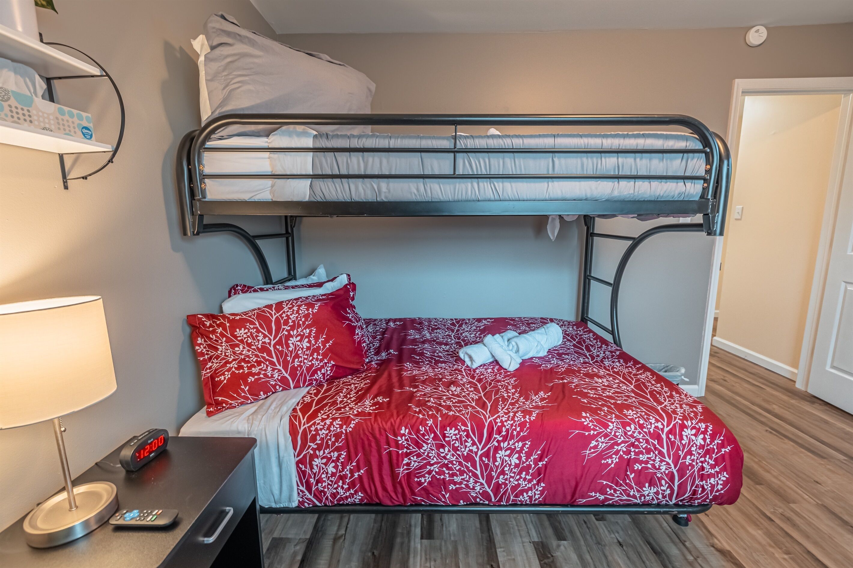 A bunk bed with a red floral bedspread, a bedside table with a lamp, and a digital clock.