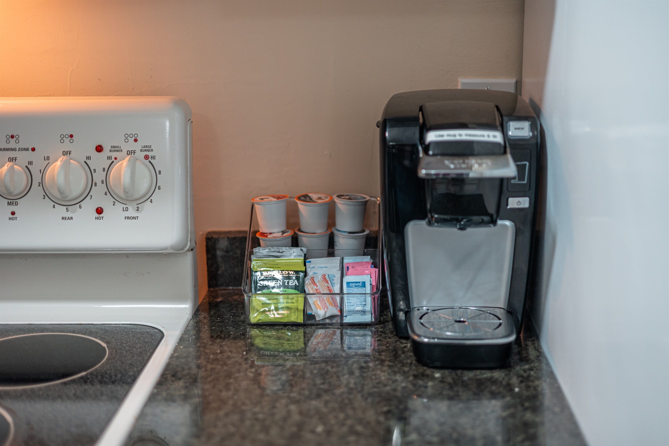 A kitchen with a coffee maker, a kettle, and a coffee pod holder.