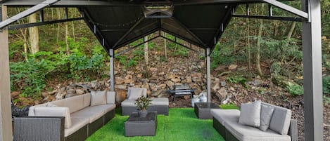 A covered outdoor seating area with wicker furniture and a stone wall backdrop.