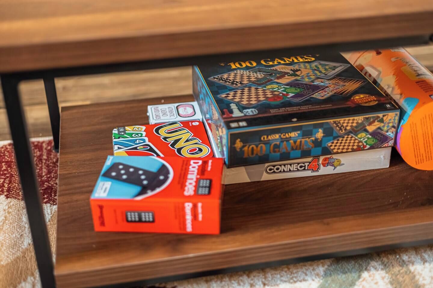 Une étagère en bois sur laquelle sont posés trois jeux de société : UNO, Connect 4 et un jeu avec un plateau à carreaux.
