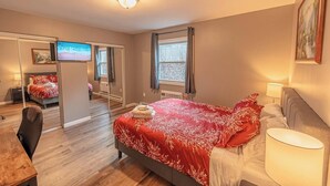 Quarto com cama, escrivaninha, cadeira, televisão e janela.