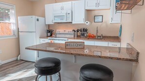 Una cocina moderna con armarios blancos, encimera de granito, un letrero de bienvenida y dos taburetes negros.