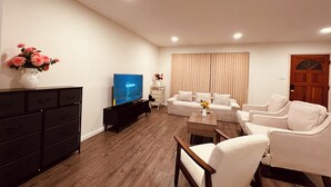 Een woonkamer met een televisie, bank, fauteuils, een salontafel en een dressoir.