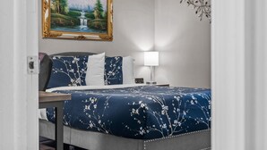 Une chambre d’hôtel avec un lit, une table de chevet, une lampe, un tableau et une branche décorative accrochée au mur.