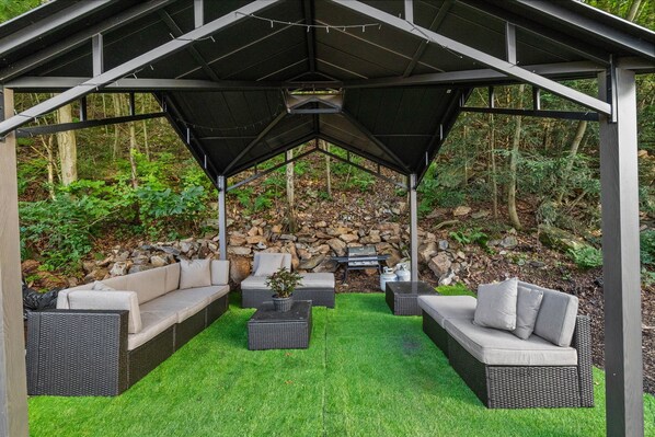 A covered outdoor seating area with wicker furniture and a stone wall backdrop.