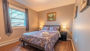 A bedroom with a bed, two bedside tables, a window with curtains, and a painting on the wall. - Near Hiking & Water Parks!*Wi-Fi*Fireplace*Patio* (Saylorsburg)