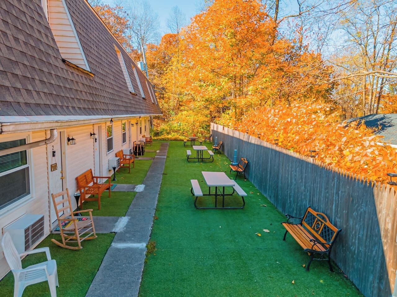 A courtyard with picnic tables and benches, surrounded by a wooden fence and trees with autumn leaves.