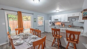 A modern kitchen with white cabinets, a microwave, and a sink. There is a dining area with a table set for six, and a wooden chair with a 'WELCOME' sign. - Near Hiking & Water Parks!*Wi-Fi*Fireplace*Patio* (Saylorsburg)