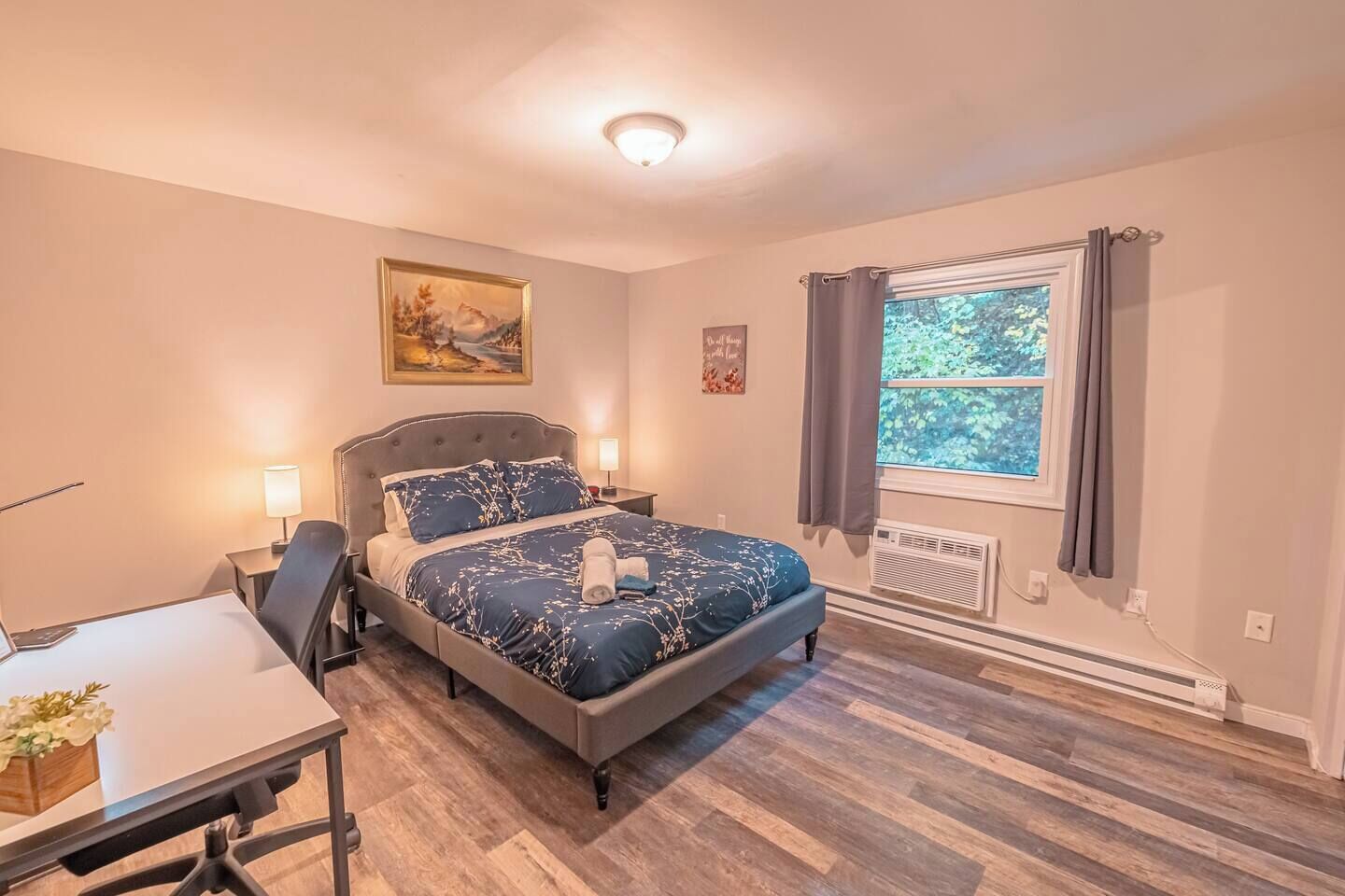 A bedroom with a bed, a desk, a chair, a window with curtains, and a painting on the wall.