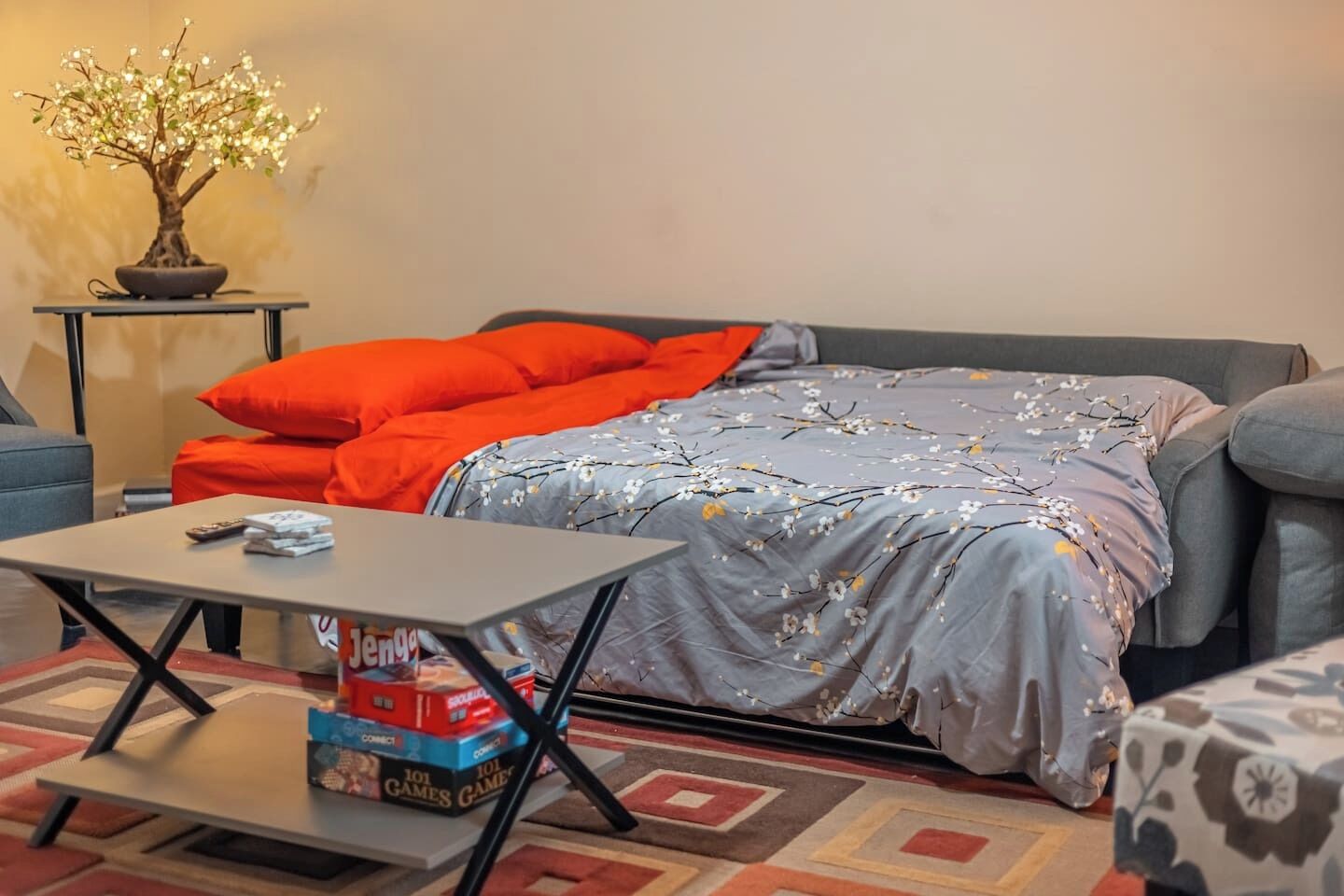 A cozy living room with a bed, a coffee table with board games, and a small table with a plant.