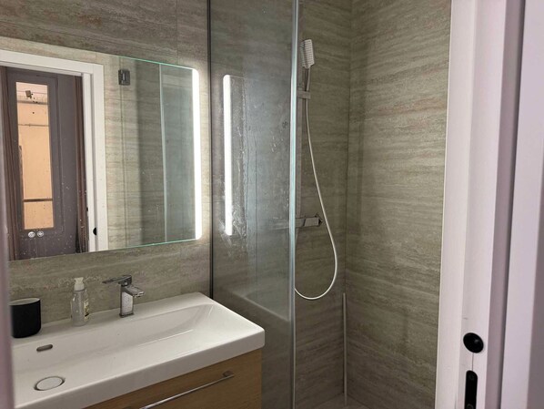 A modern bathroom with a glass-enclosed shower, a white sink, and a mirror above it.