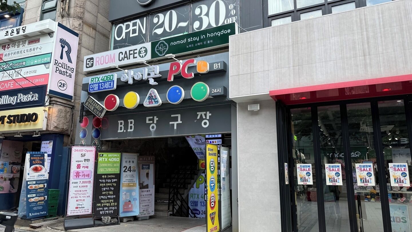 A storefront with various signs, including a Rolling Pasta sign, a PC store, and a Room Cafe.