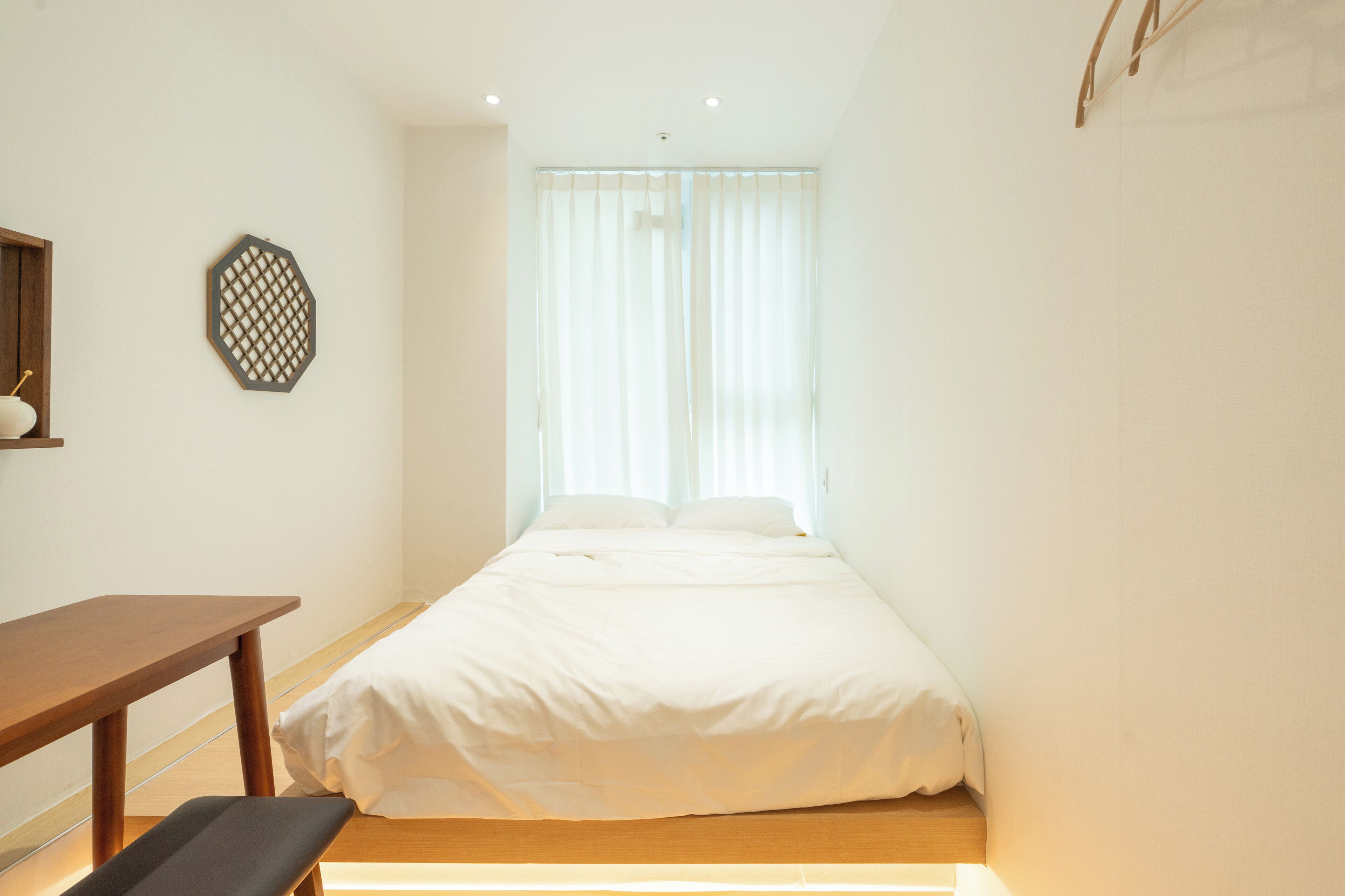 A bedroom with a bed, a wooden bench, a small table, and a decorative wall piece.