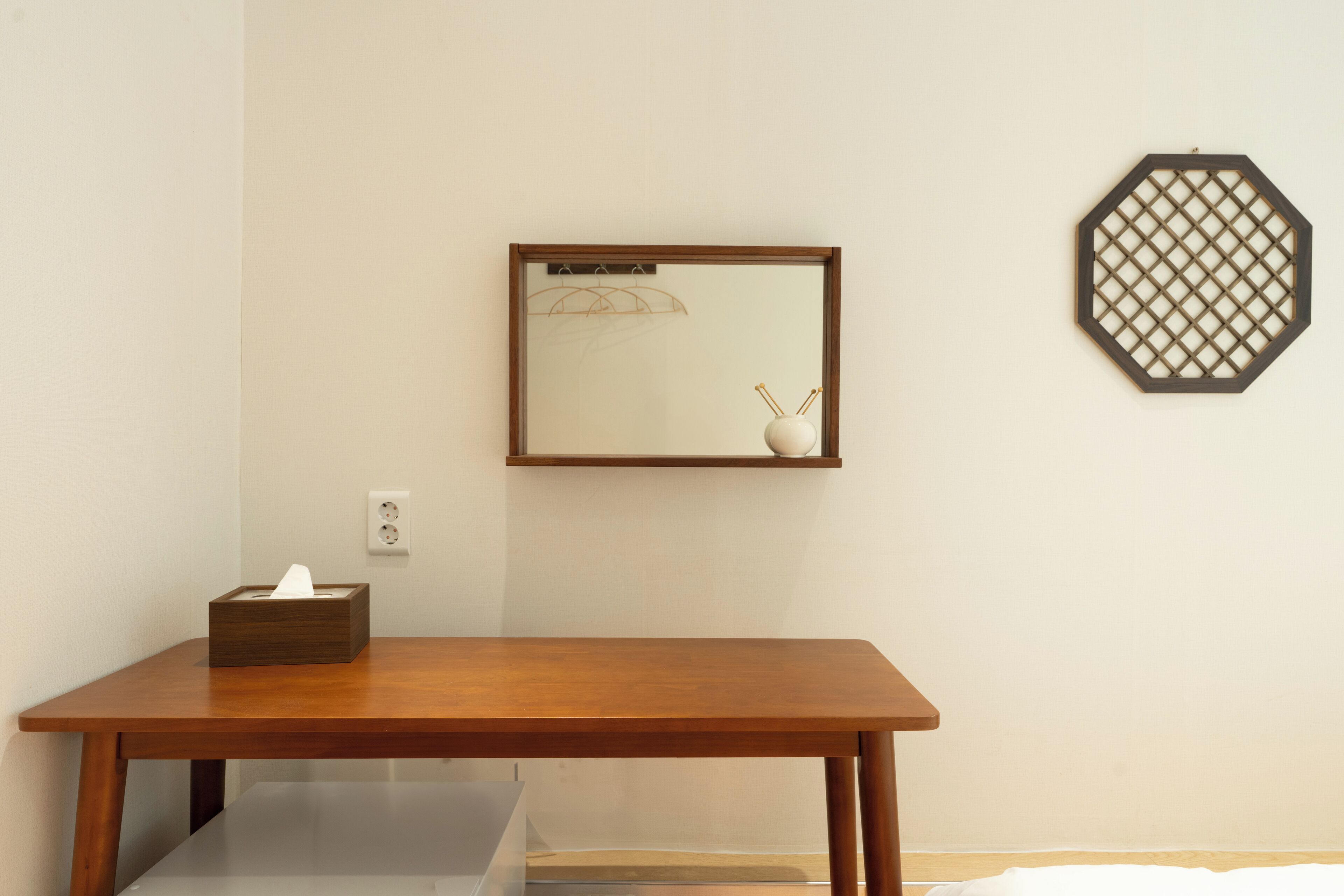Una mesa de madera con una caja de pañuelos, una obra de arte enmarcada y un objeto decorativo octogonal en la pared.