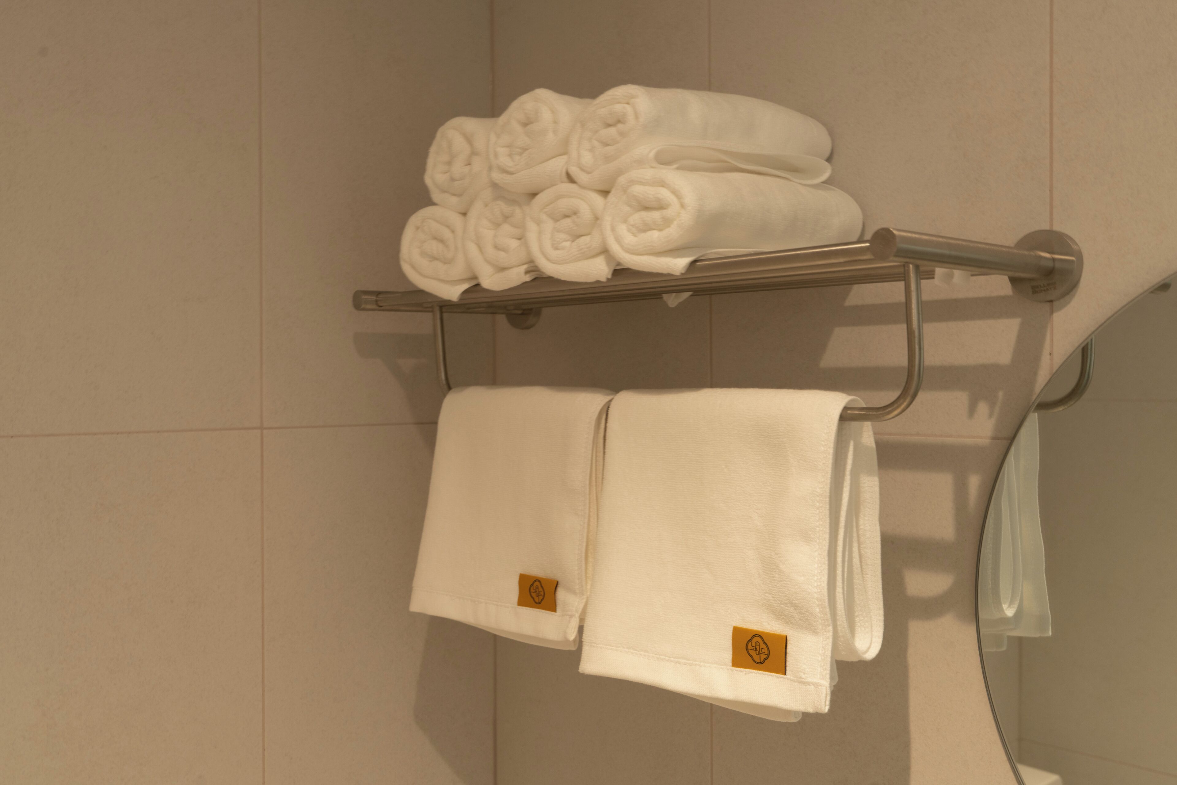 A bathroom with a towel rack holding neatly folded towels and a rolled towel.