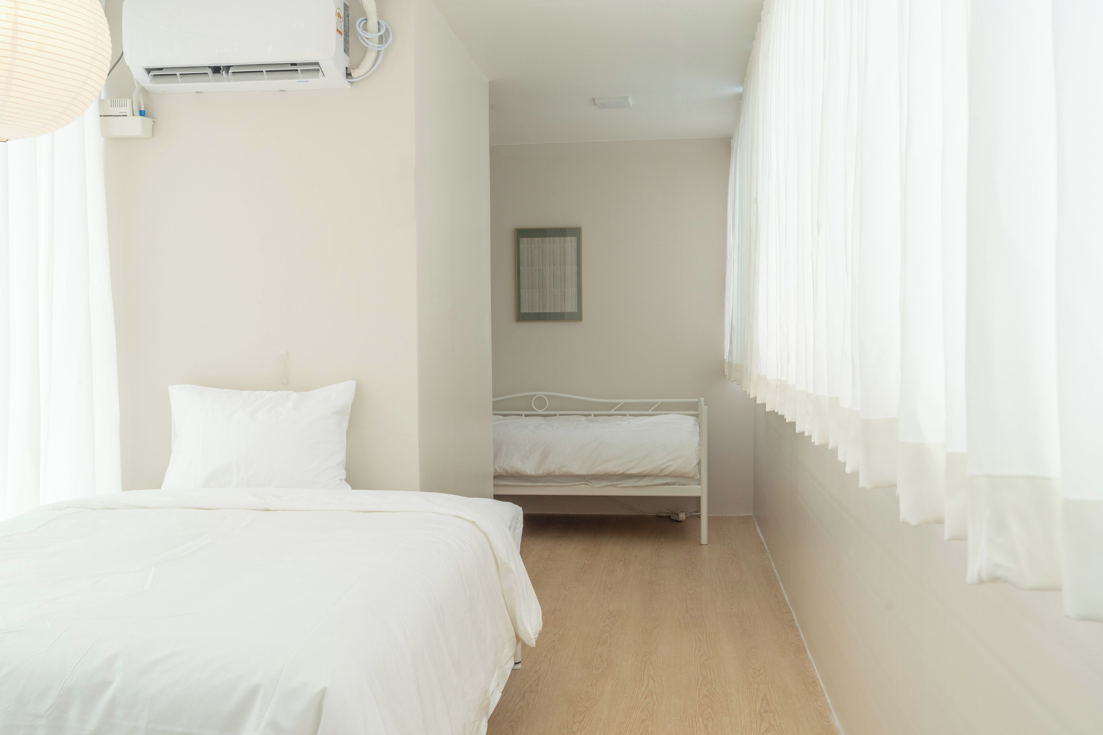 Ein Schlafzimmer mit zwei Betten, einer Wandklimaanlage und einem gerahmten Bild an der Wand.