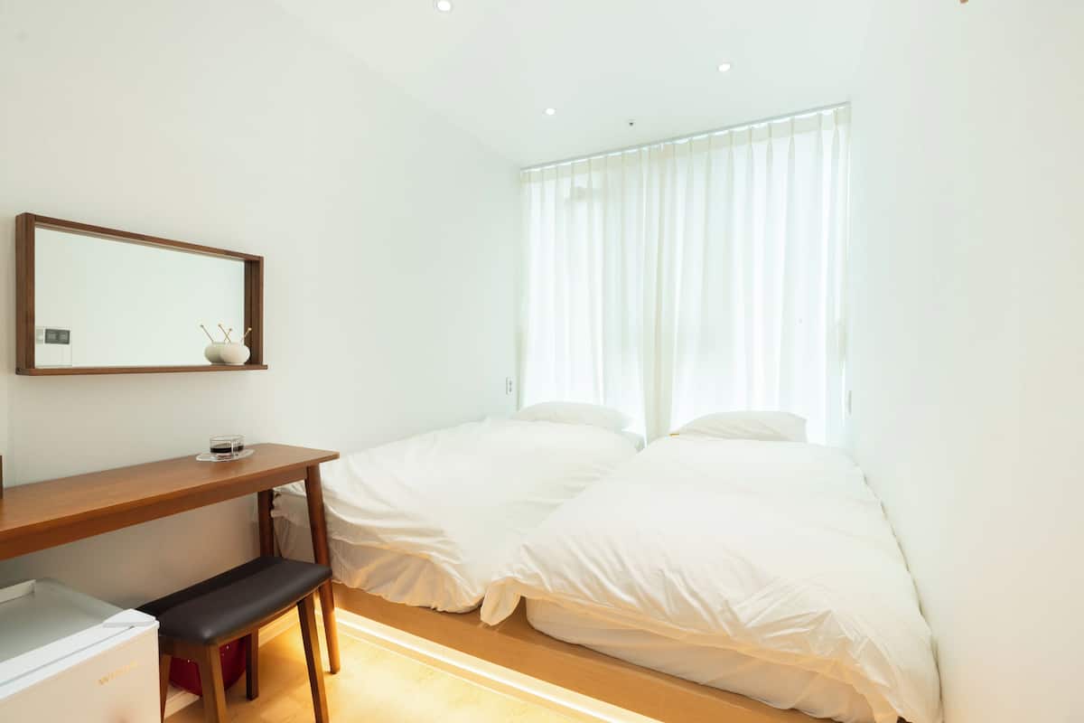 A bedroom with two beds, a wooden desk, a bench, a small table, and a mirror.