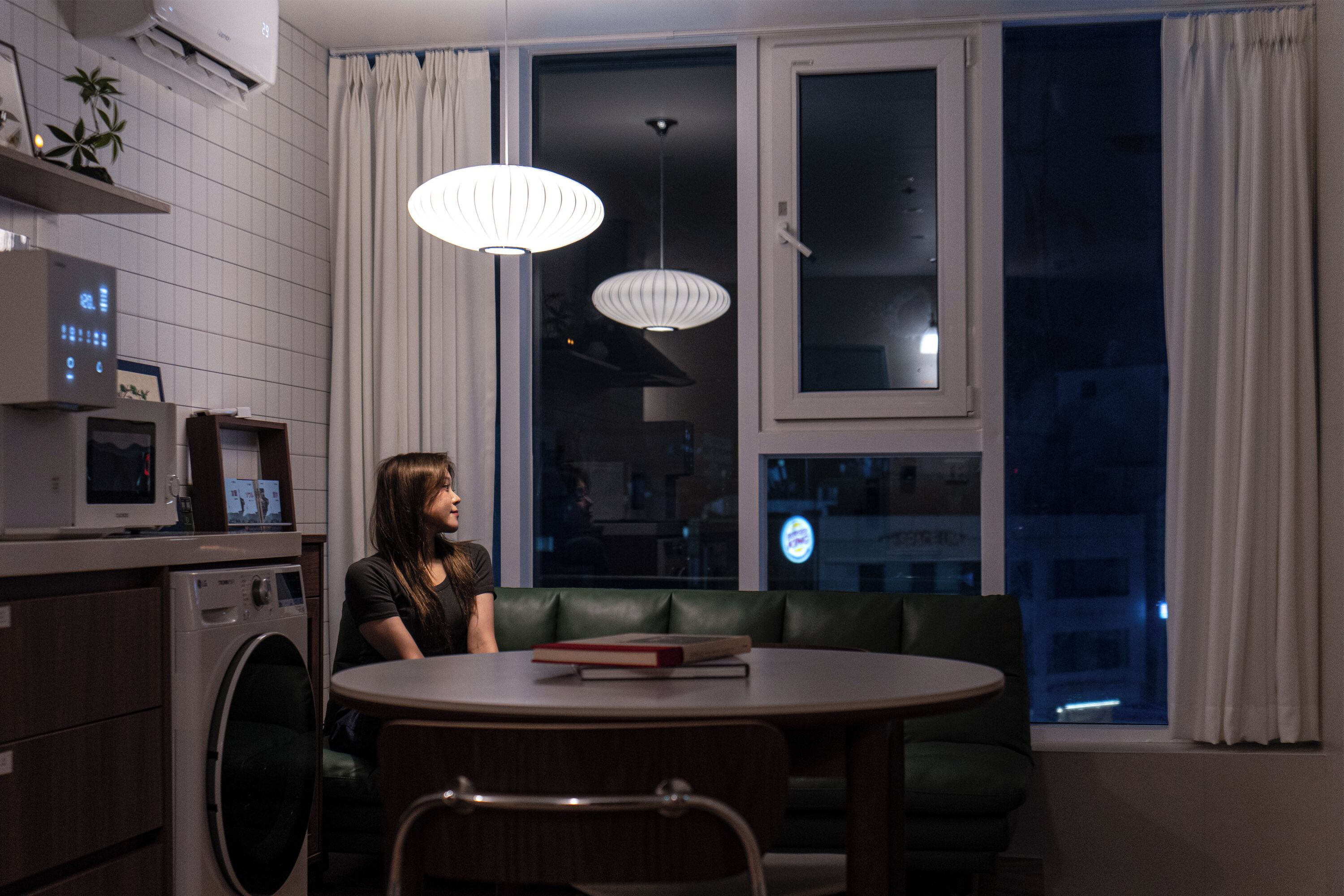 A modern kitchen with a microwave, washing machine, and a dining area with a table and green sofa.