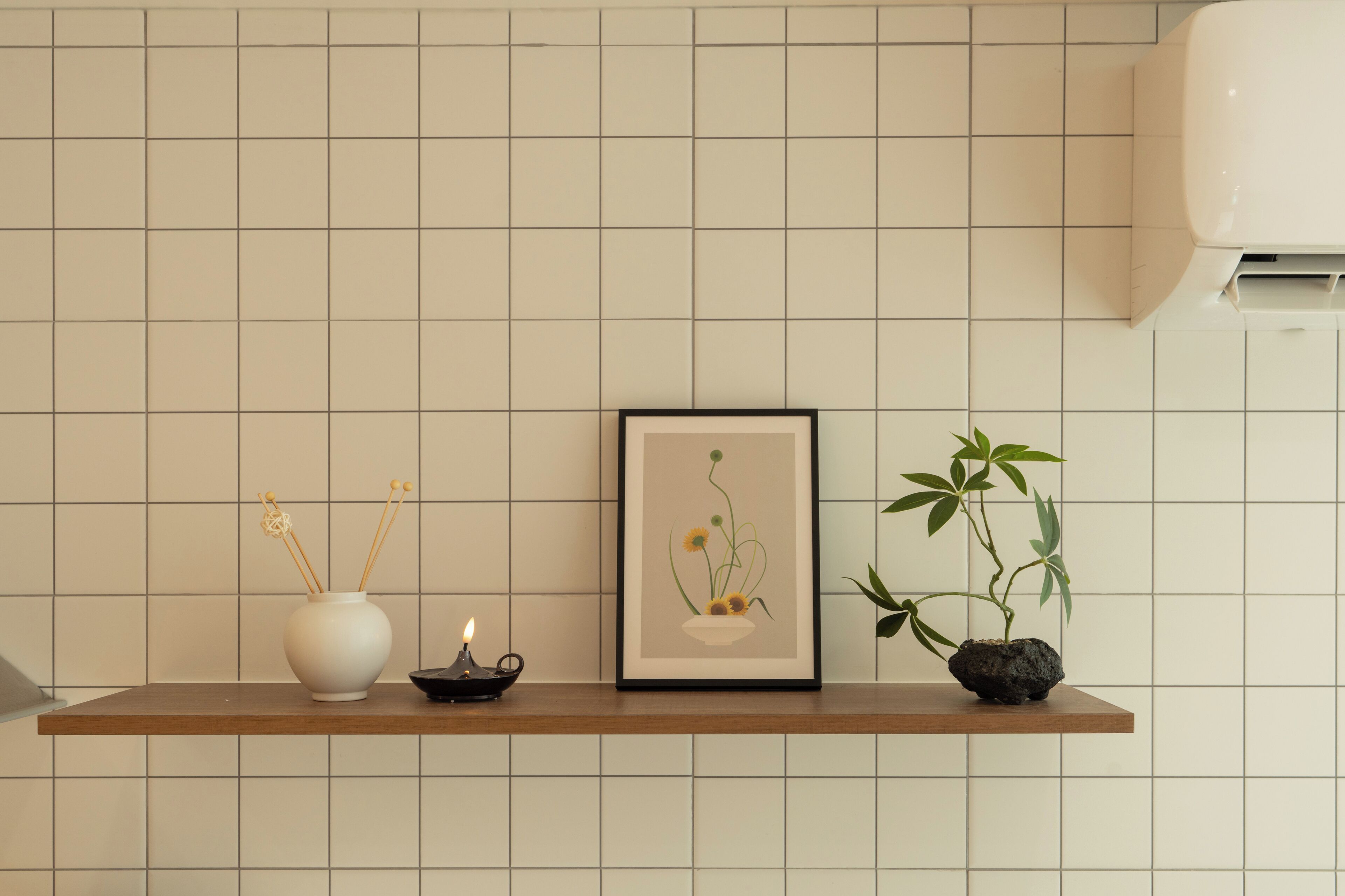 A shelf with a white vase, a framed picture, a small candle, and a potted plant.