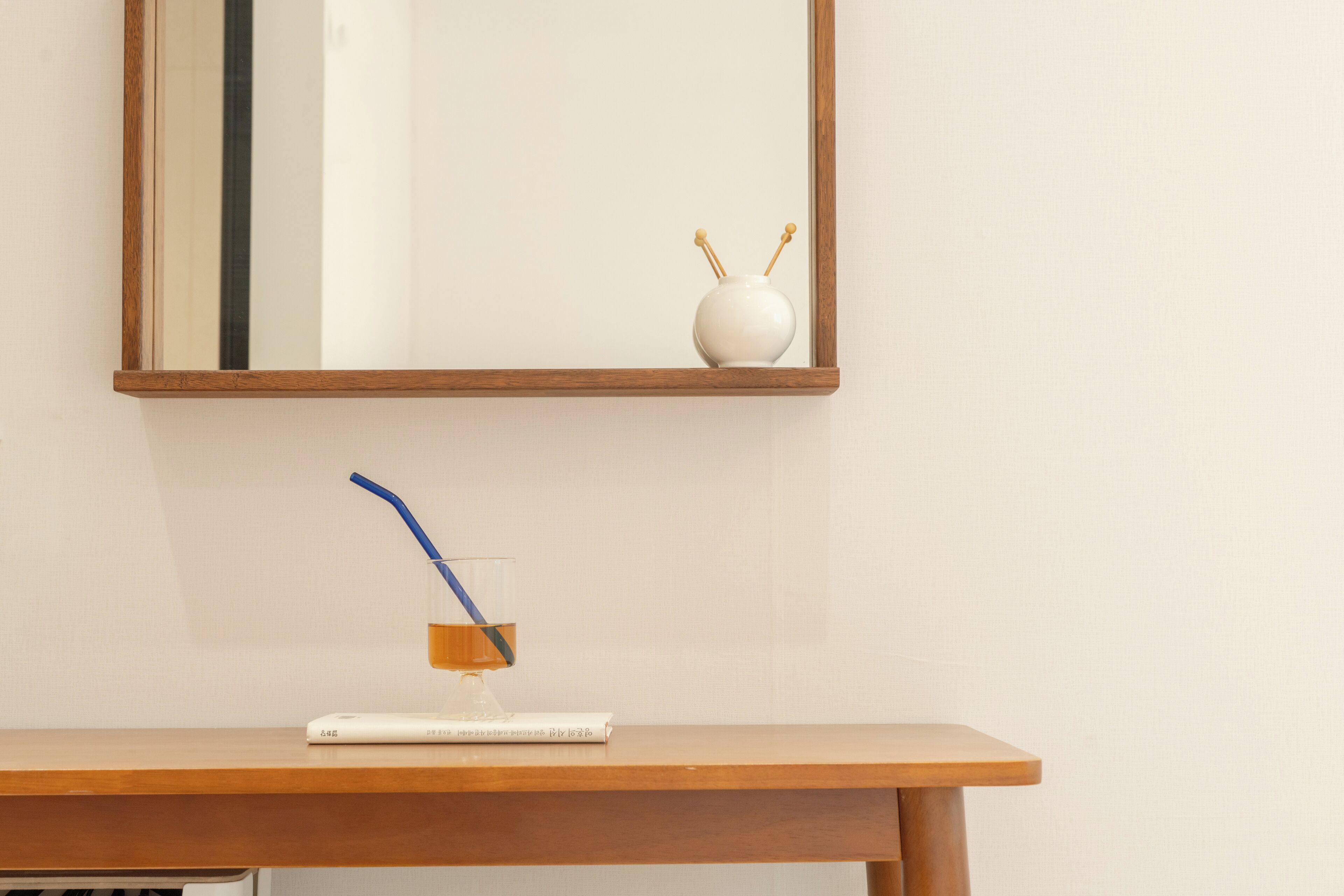 A wooden desk with a glass containing a blue straw and a white book.