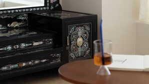 Un buffet noir orné de motifs décoratifs, un verre contenant une boisson et un livre ouvert sur une table en bois.