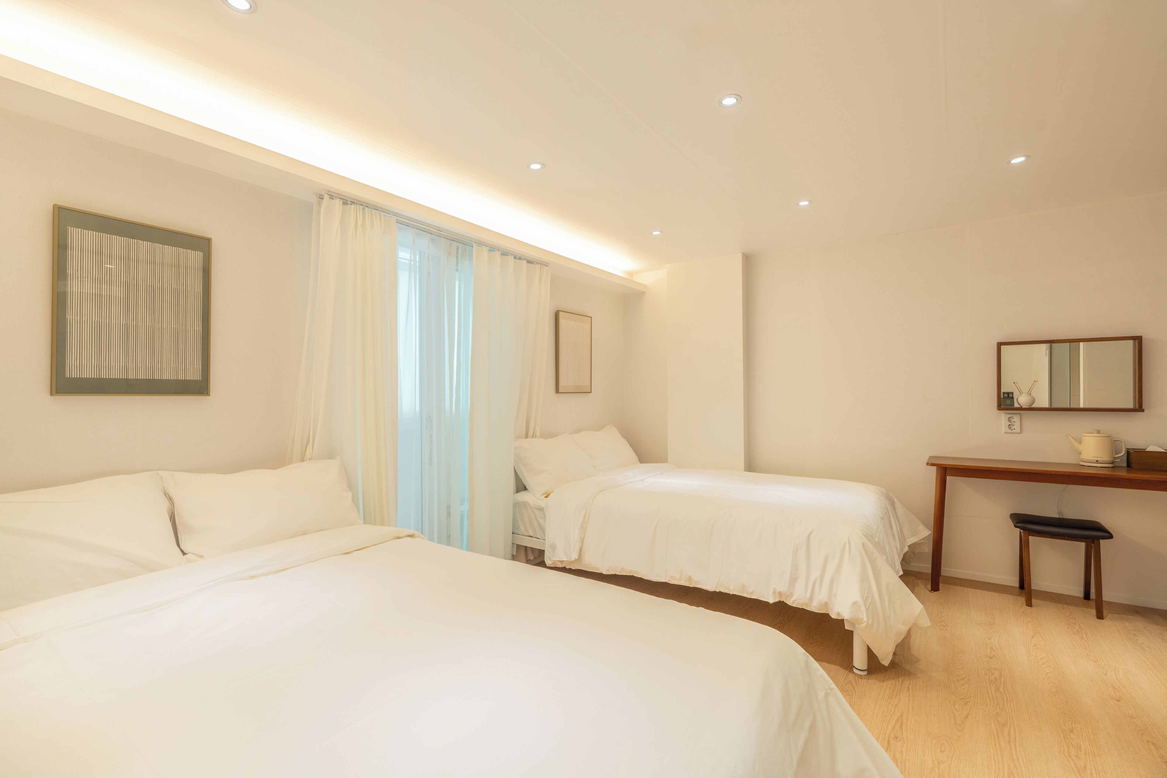 A hotel room with two beds, a desk, a chair, and a mirror.