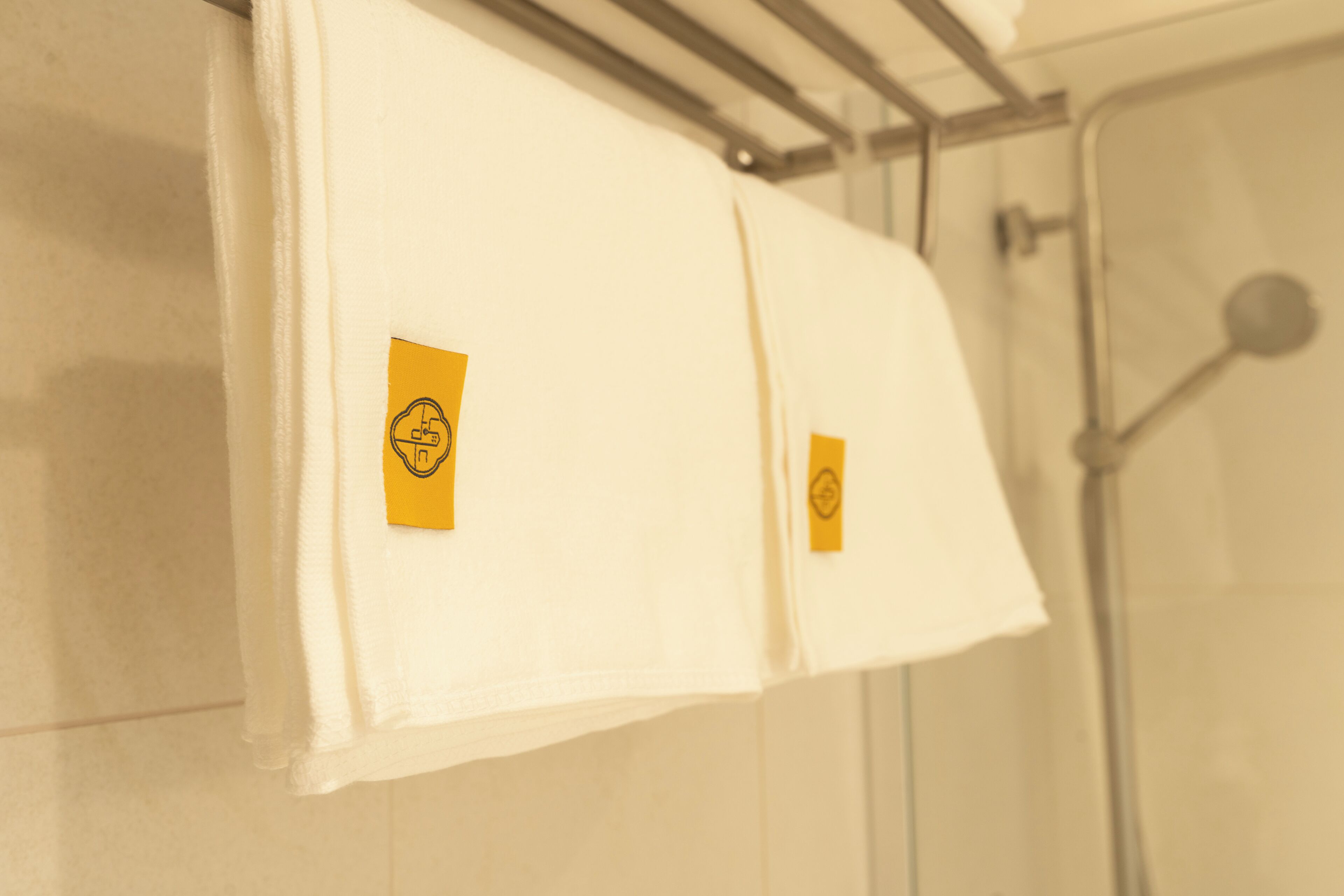 Une salle de bain avec deux serviettes blanches suspendues à un porte-serviettes, chacune étant munie d’une étiquette jaune.