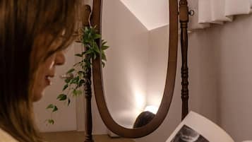 A person reading a book in a room with a wooden chair and a mirror.