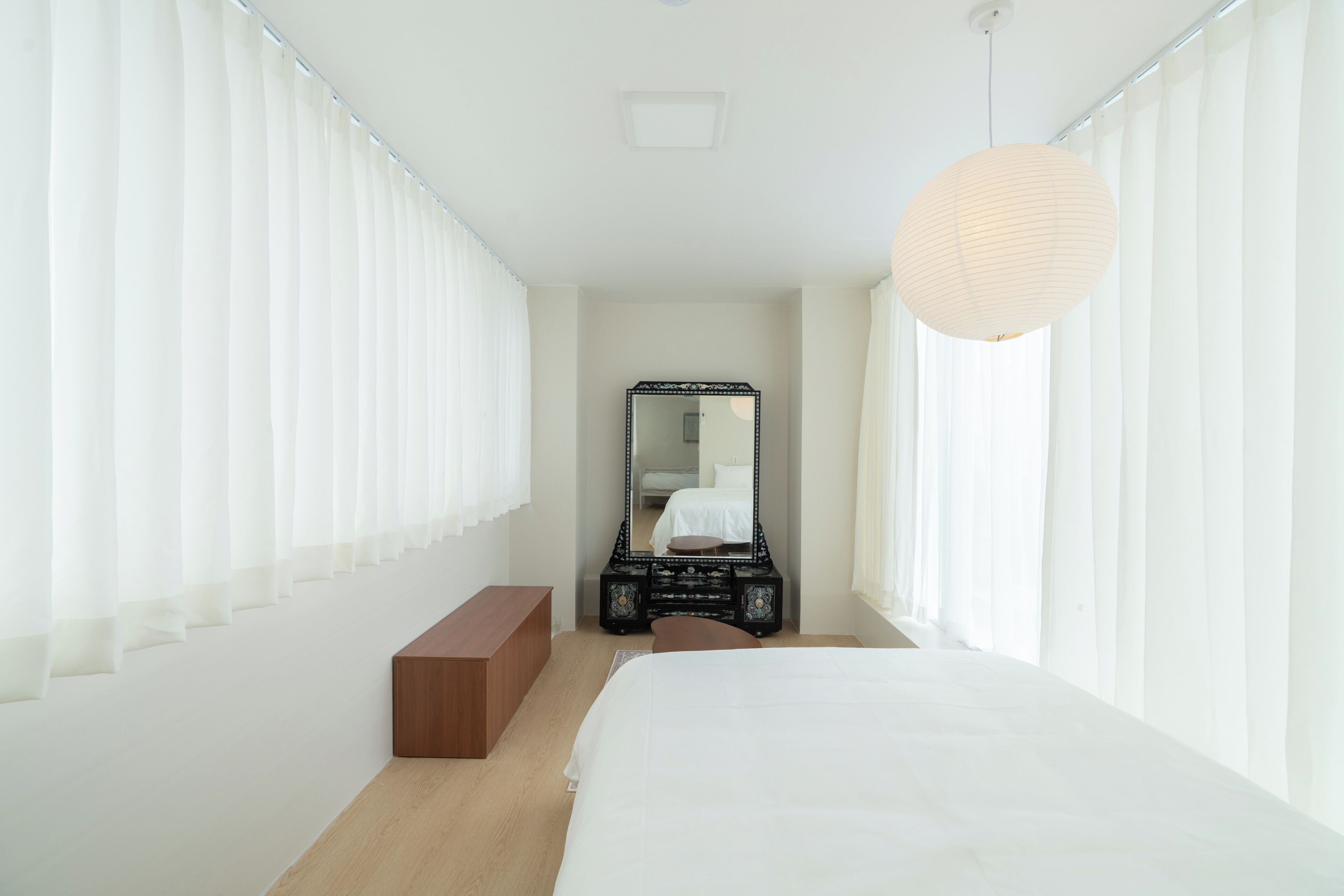 Une chambre à coucher avec un lit, un banc en bois, un miroir et un luminaire suspendu.