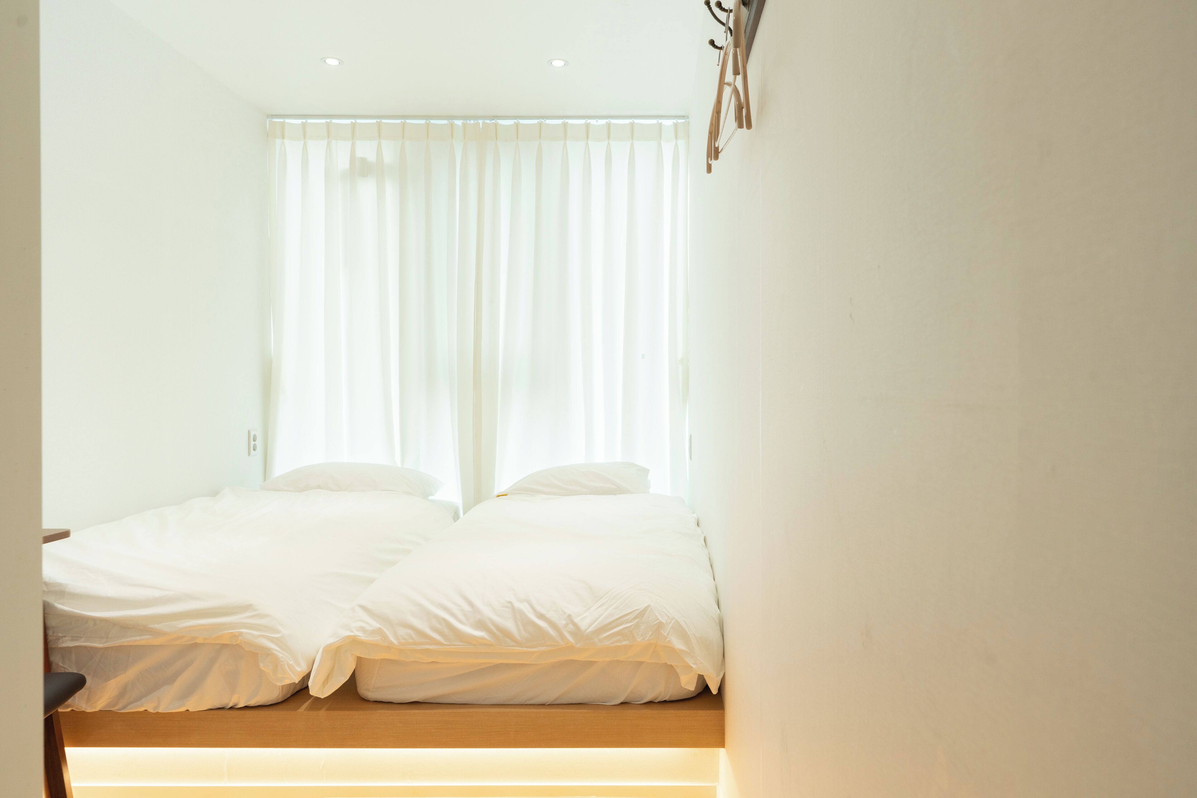 Quarto com cama, cortinas brancas e cabeceira de madeira.