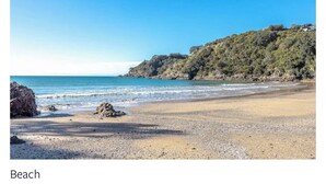 A beach with a rocky shoreline, calm sea, and a clear sky. - Tawa Street, Oneroa - Blue Sky Retreat - Spa pool (waiheke island)
