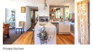 A private kitchen with a marble island, wooden flooring, and a view of the living area. - Tawa Street, Oneroa - Blue Sky Retreat - Spa pool (waiheke island)