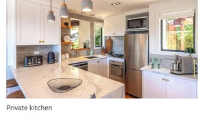 A private kitchen with white cabinets, a marble countertop, stainless steel appliances, pendant lighting, and a window providing natural light. - Tawa Street, Oneroa - Blue Sky Retreat - Spa pool (waiheke island)