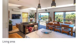 A modern living area with a dining table, chairs, a sofa, and a TV. - Tawa Street, Oneroa - Blue Sky Retreat - Spa pool (waiheke island)