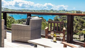 Eine Terrasse mit Korbmöbeln und einem Tisch, mit Blick auf eine malerische Wasserlandschaft und grüne Vegetation.