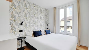 Un dormitorio con una cama grande, dos mesitas de noche, un papel tapiz estampado, una ventana con cortinas y vistas al exterior.