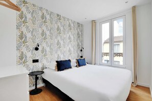 Un dormitorio con una cama grande, dos mesitas de noche, un papel tapiz estampado, una ventana con cortinas y vistas al exterior.