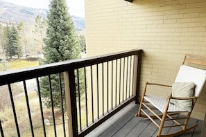 A balcony with a wooden rocking chair, a brick wall, and a view of trees and mountains.