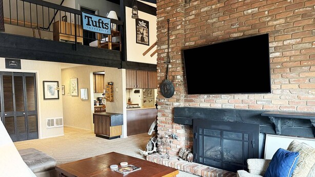 A loft-style living area with a fireplace, a television mounted on the wall, and a sign reading "Tufts University". - Great Rates and Month Stays Available! Slope Views, Near Mountain/Base/Eat, Spacious with Loft (Steamboat Springs)