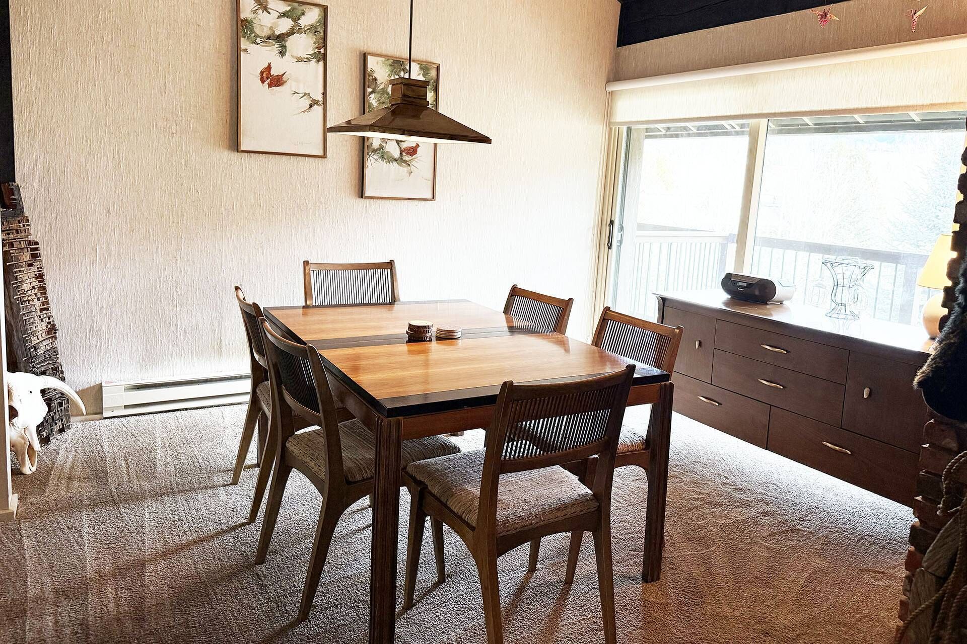 Ein Essbereich mit einem Holztisch und Stühlen, einer Pendelleuchte und Bildern an der Wand.