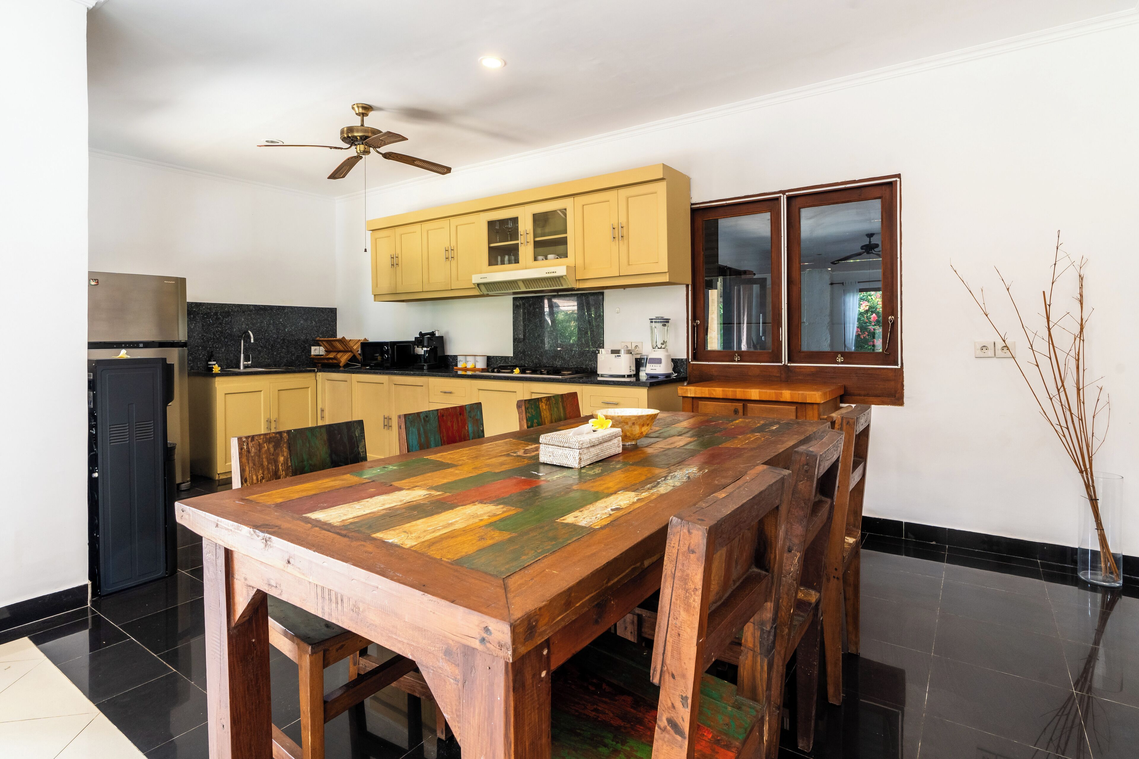 A modern kitchen with a wooden dining table, yellow cabinets, and a black countertop.