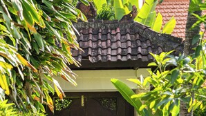 Een houten poort in traditionele stijl met een pannendak, omringd door weelderig groen en een betonnen pad er naartoe.